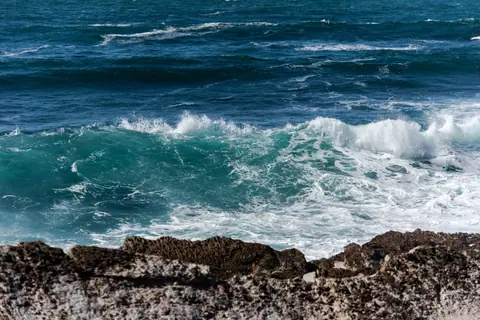 Energetic ocean waves crashing against rocky coast under clear skies.