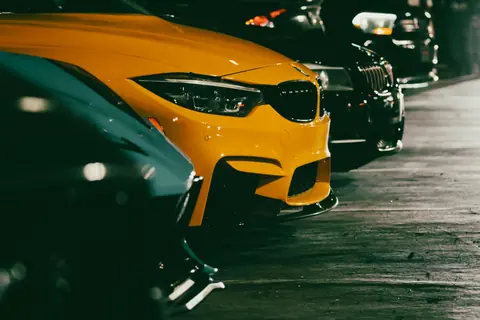 Close-up view of multiple sports cars parked in a dimly lit parking lot at night.
