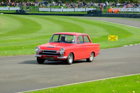 Vibrant red Ford Cortina racing at Goodwood, showcasing vintage car charm in England.