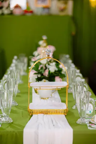 A sophisticated table arrangement featuring a gold tiered server and floral centerpiece on a green tablecloth.