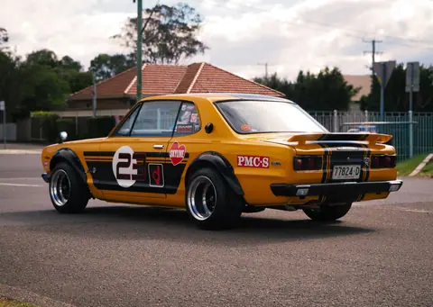 A classic yellow Nissan Skyline on display outdoors, showcasing motorsport heritage and style.