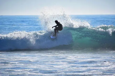 Silhouette of a surfer skillfully riding a wave under bright sunlight at the beach.