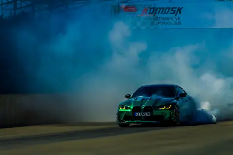 A green car drifting amidst smoke on a race track during a motorsport event.