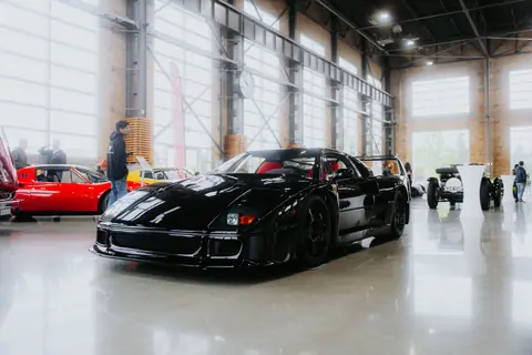A glossy black sports car showcased in an industrial indoor auto event with modern architecture.