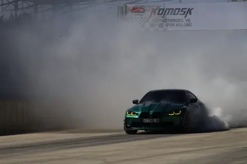 A green sports car performing a drift on a track, surrounded by smoke.