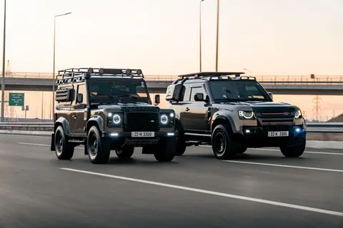 Two Land Rover Defenders driving side-by-side on a city highway in Erbil, Kurdistan at sunset.
