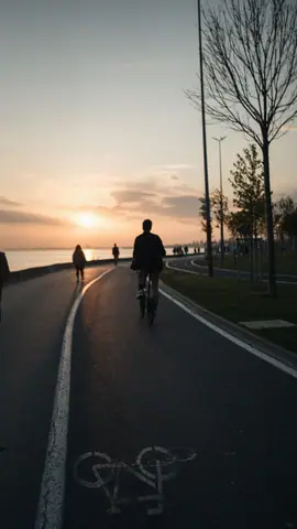 People biking and walking at sunset along a scenic waterfront path.
