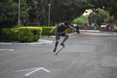A skilled skateboarder mid-air performing a trick on a street in a leafy park.