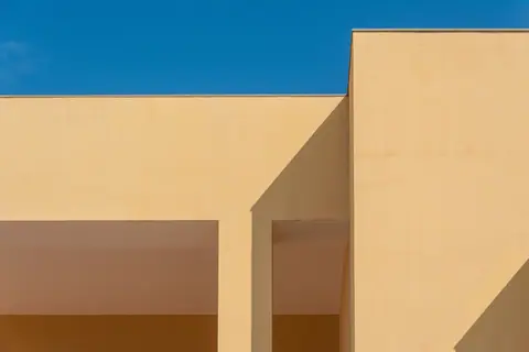 Minimalist architecture with geometric shadows and clear blue sky creates a striking abstract composition.