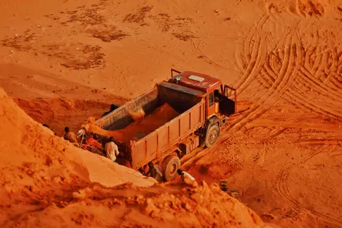 A dump truck and workers at a red soil extraction site, highlighting industrial work.