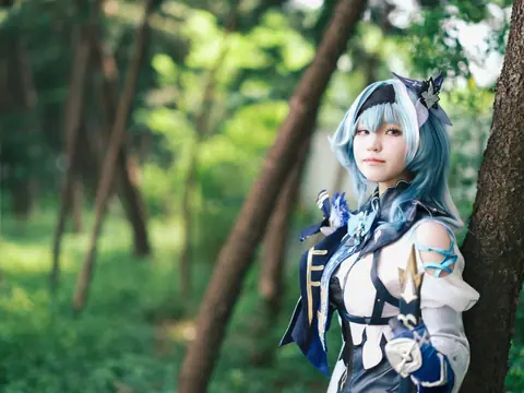 A cosplayer dressed in a blue themed costume poses in a lush forest.