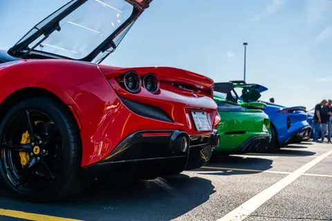 Colorful luxury sports cars lined up in an outdoor parking lot under a clear blue sky.