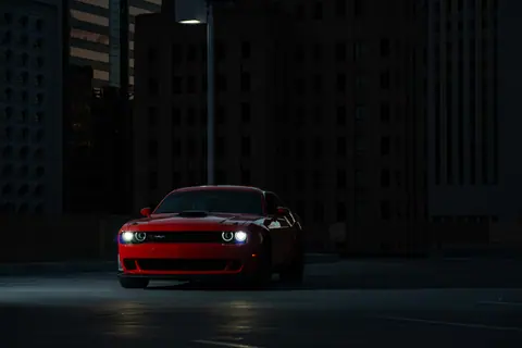 Dramatic shot of a red sports car parked at night in an urban setting, illuminated by streetlight.