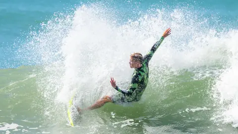 Surfer skillfully rides a wave, creating a splash in the vibrant blue ocean.