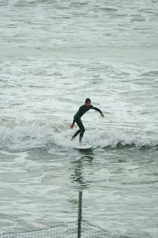 A surfer skillfully navigates small waves on an overcast day, showcasing balance and determination.