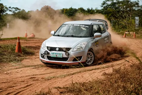 Silver rally car speeding through a dirt track, creating a dramatic dust cloud.