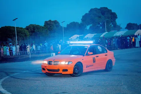 Vibrant orange car drifting on track with a crowd in the background.