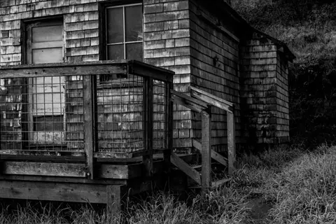 Black and white photo of an old, abandoned rustic house's exterior.