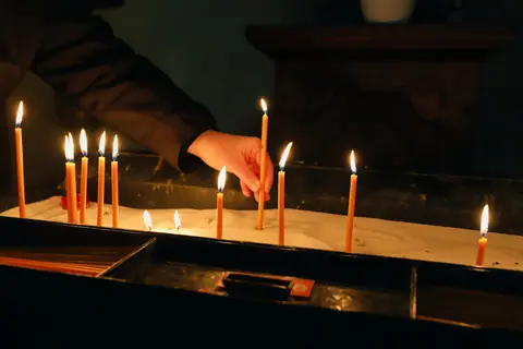 A hand lights slender candles in a church for prayer or reflection.