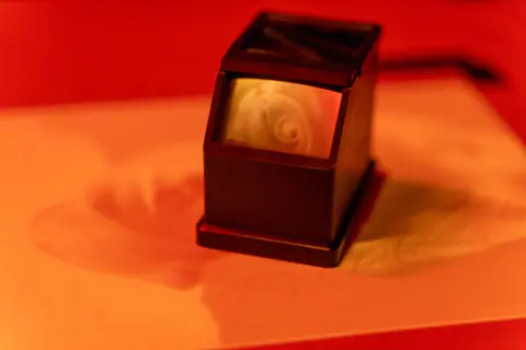 A vintage film scanner set against an orange-red background, exuding a warm, nostalgic vibe.