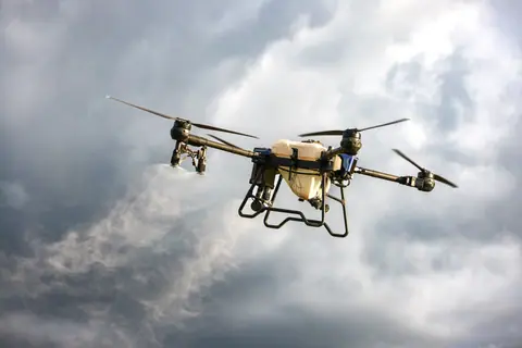 A drone dispersing mist in a cloudy sky, showcasing agricultural technology innovation.