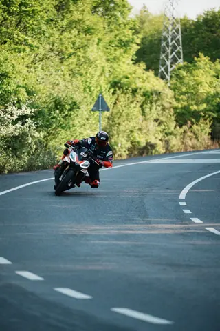A motorcyclist speeds through a curve on a tree-lined road, showcasing thrilling speed and agility.
