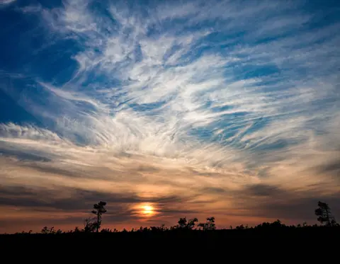 Captivating sunset over a silhouette landscape with striking cloud formations and a vivid sky.
