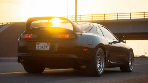 Rear view of a black Toyota Supra parked on city streets during sunset.