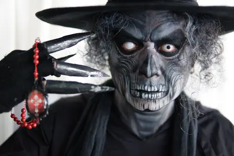 Close-up of a person in skeleton makeup and costume, holding beads with claws.