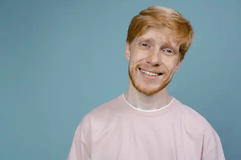 Close-up of a happy redheaded man smiling with a light blue background.