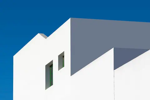 A modern building with white walls and green windows against a clear blue sky. Minimalist architecture style.