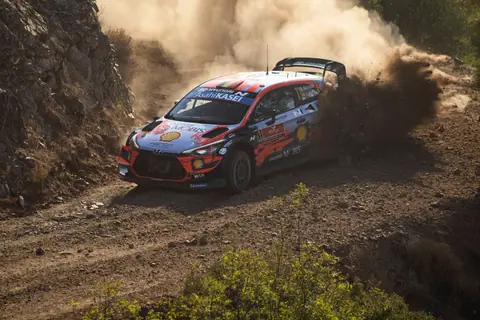 High-speed rally car navigating a dusty dirt road, showcasing endurance and precision driving.