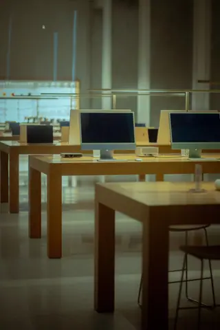 Empty computer store with wooden tables and modern desktop computers displayed.
