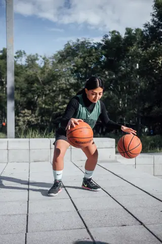 A young woman skillfully dribbling two basketballs on a sunny day in Mexico City.