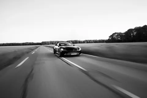 Black and white image of a luxury sports car speeding on an open road.