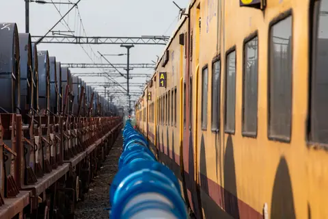 View of parallel trains and blue pipes at a railroad yard, showcasing industrial transportation.