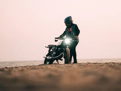 A biker rides a motorcycle on a sandy beach during sunset, evoking a sense of adventure and freedom.