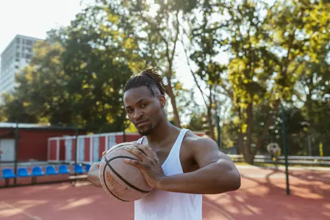 Confident young man holding a basketball on an outdoor court, ready to play.
