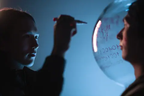 Person writing on a transparent sphere against a blue background with focused expression