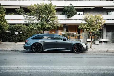 Stylish grey car parked by trees on a modern city street with a residential building backdrop.