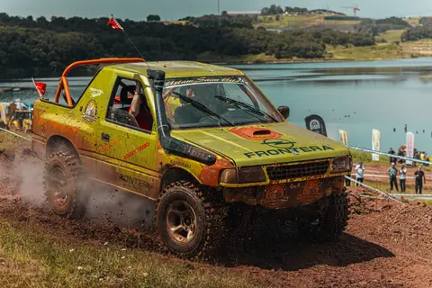 A dynamic scene of an offroad vehicle racing on a muddy track alongside a picturesque lake backdrop.