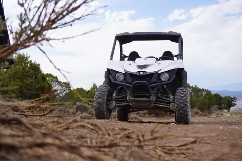 White off-road utility vehicle conquering rugged terrain outdoors under a bright sky.