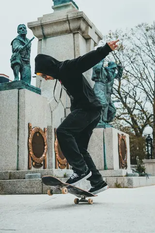 Skateboarder performing a trick near statues in a park, showcasing skill and style.
