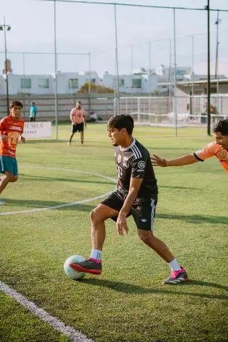 Teenagers playing a competitive game of soccer on an outdoor field during the day.