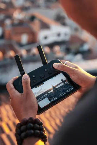 Close-up of a person using a drone controller, capturing a cityscape at sunset.