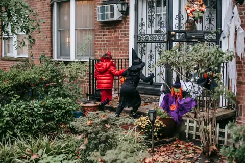 Little girls in red and black costumes with buckets walking on porch of house before asking treats during Halloween