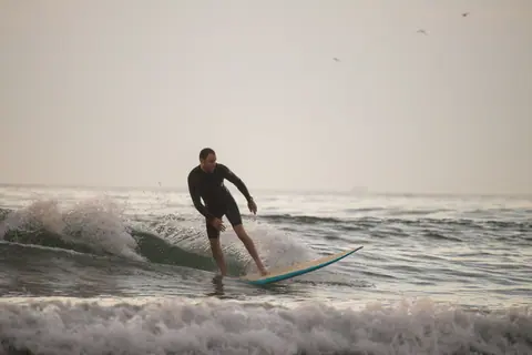 A man surfing gracefully on a wave during sunrise, showcasing a serene ocean adventure.