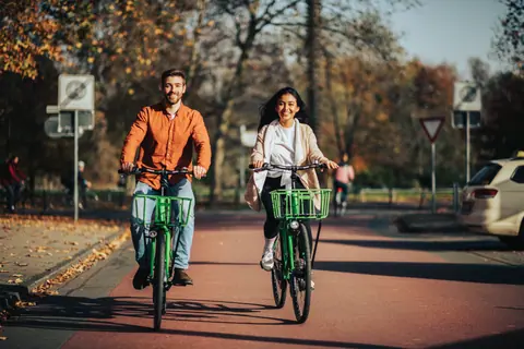 Man and woman riding bicycles on a sunny autumn street in a park.