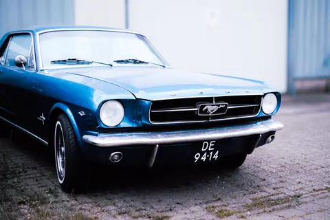 A striking photo of a classic blue Ford Mustang parked outdoors with visible license plate.