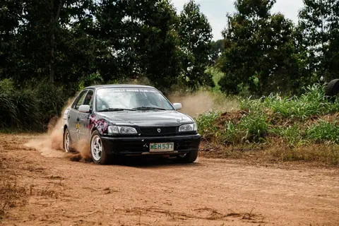 Rally car speeding on a dirt track in Baras, Calabarzon, Philippines, surrounded by greenery.